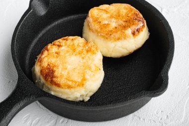 Peynirli kekler, tuzlu süzme peynirli krepler, dökme demir tavada tavada, beyaz taş masa arkasında.