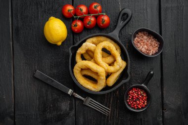 Kızarmış Calamari ya da soğan halkaları dökme demir tavaya, siyah ahşap masa arka planına, üst görünüm düz yere, metin için kopyalama alanına ayarlı.