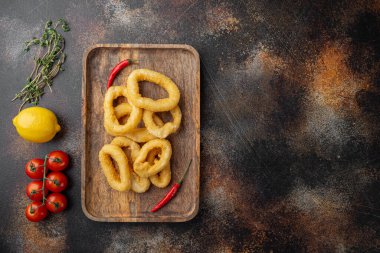Ekmek kırıntıları içinde çıtır kalamar halkaları servis panosunda, eski koyu kırsal masa zemininde, üst görünüm düz yatağında, metin için kopyalama alanı ile