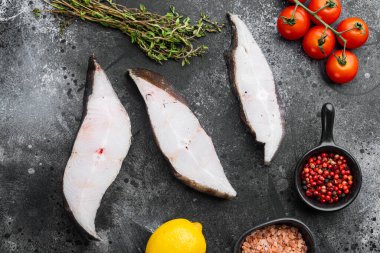 Çiğ taze halibut balığı bifteği seti, malzemeler ve biberiyeler, siyah taş masa zemininde, üst manzara düz