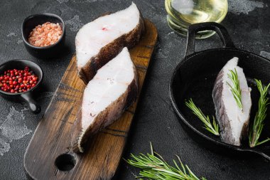 Soğuk halibut biftekleri, malzemeler ve biberiyeli, siyah taş masa arkasında.