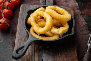 Dilimlenmiş kalamar tapası dökme demir tavaya yerleştirilmiş halkalar halinde, eski, siyah ahşap masa arka planında.