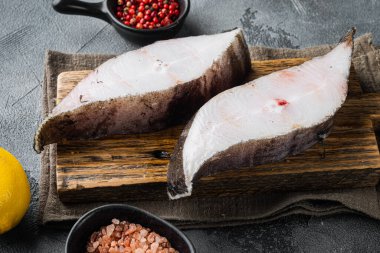 Çiğ halibut, tuzlu su balığı bifteği seti, malzemeler ve biberiye otları, gri taş masa arkasında.