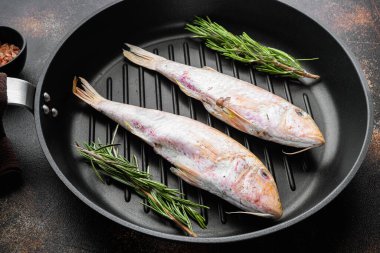 Çiğ surmullet tüm deniz ürünleri seti, malzemeler ve otlar dökme demir tava tava üzerinde, eski koyu rustik masa arka planı