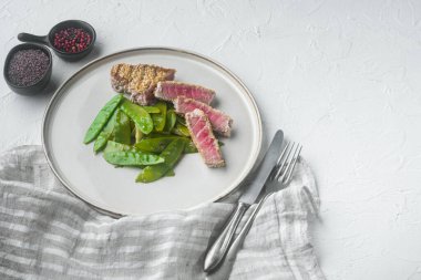 Susamlı ızgara ton balığı bifteği ve taze soğan ve bezelyeli soya sosu, tabakta, beyaz taş zemin üzerinde, metin için telif alanı ve boşluk.