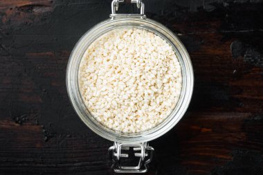 Beyaz susam tohumları seti, cam kavanoz içinde, eski siyah masa arkaplanı üzerinde, üst görünüm düz yatıyordu