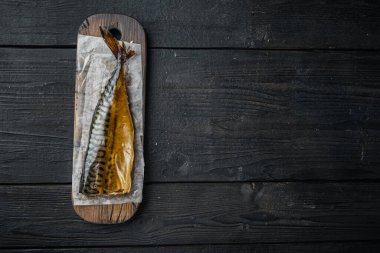 Tütsülenmiş balık uskumrusu, siyah ahşap masa arkaplanı üzerinde, üst görünüm düz metin alanı için fotokopi alanı ile yatıyordu