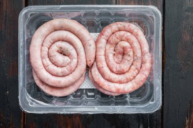 Çiğ et sosisi seti, eski koyu ahşap masa zemininde, plastik pakette, üst görünüm düz