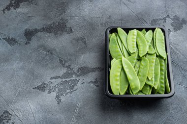 Organik Yeşil Şekerli Bezelyeler, plastik kabın içinde, gri taş zemin üzerinde, metin için metin alanı ve boşluğu ile hazır.