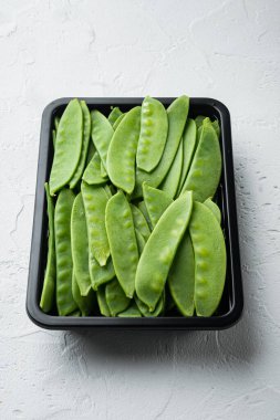 Sağlıklı bezelye seti, plastik kabın içinde, beyaz taş arka planda.