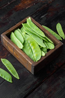 Şekerli bezelyeler, taze olgun bebek kabukları, tahta kutuda, eski, siyah tahta masa arkasında.