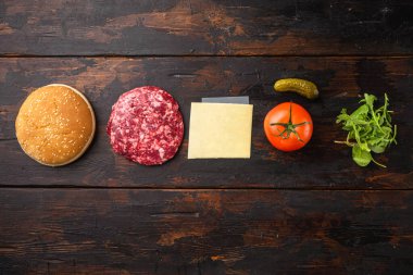 Ev yapımı hamburger. Çiğ et köfteleri, diğer malzemelerle birlikte susamlı çörekler, eski koyu ahşap masa arkaplanı üzerinde, üst görünüm düz, metin için kopya alanı ile