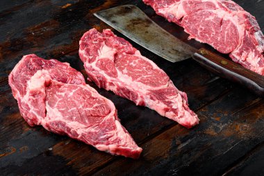 Çiğ mermer et, biftek, pirzola. Siyah Angus kaburga seti, eski siyah ahşap masa arkasında.