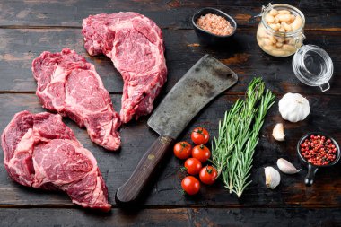 Çiğ et, Ribeye bifteği, malzeme seti ile Black Angus Prime eti ve eski kasap satır bıçağı, eski siyah ahşap masa arka planında