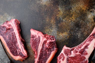 Siyah Angus Prime çiğ biftek seti, tomahawk, t kemik veya biftek ve kulüp biftek, eski koyu rustik arka planda, üst görünüm düz, metin için yer