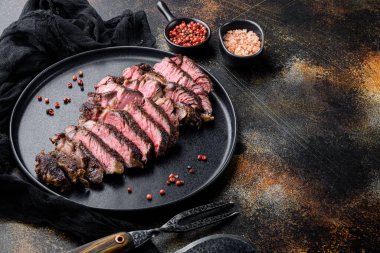 Dilimlenmiş biftek kaburgası orta az pişmiş, tabakta, eski koyu kırsal arka planda, metin için fotokopi alanı ile.