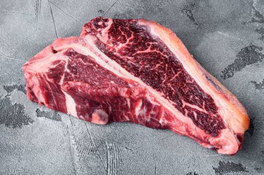 Klasik taze sığır eti bifteği seti, T kemiği kesimi, gri taş arka planda.
