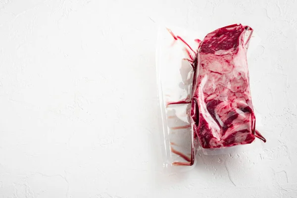 Pack with fresh beef steak cut for sous vide in vacuum plastic market bag set, on white stone  background, with copy space for text