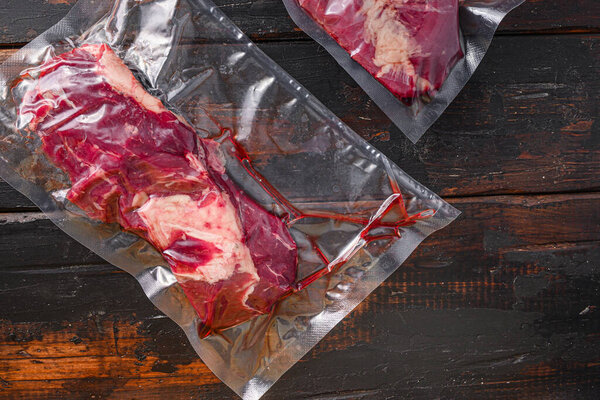 Vacuum packed Chuck roll  beef steak on dark old wooden background, close up top view