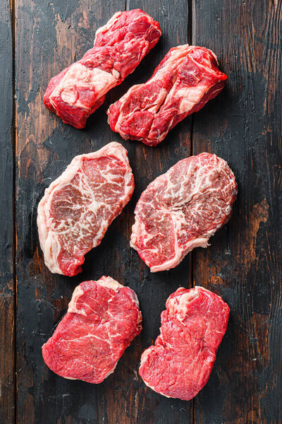 Variety of fresh Black Angus Prime raw beef steakes on old rustic dark wooden background, top view