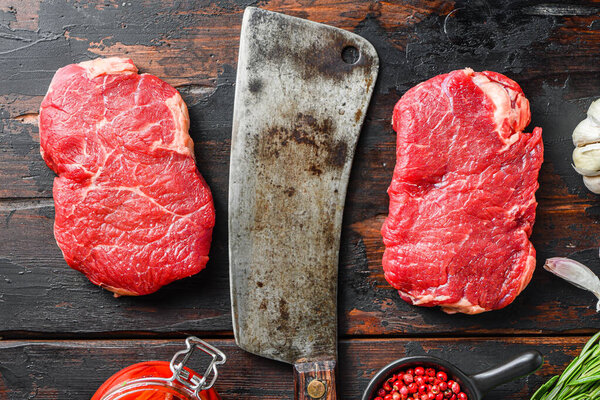 Rump steak organic meat cut, raw marbled beef steak, with old butcher knife cleaver, and seasonings  On dark wooden rustic table,  top view