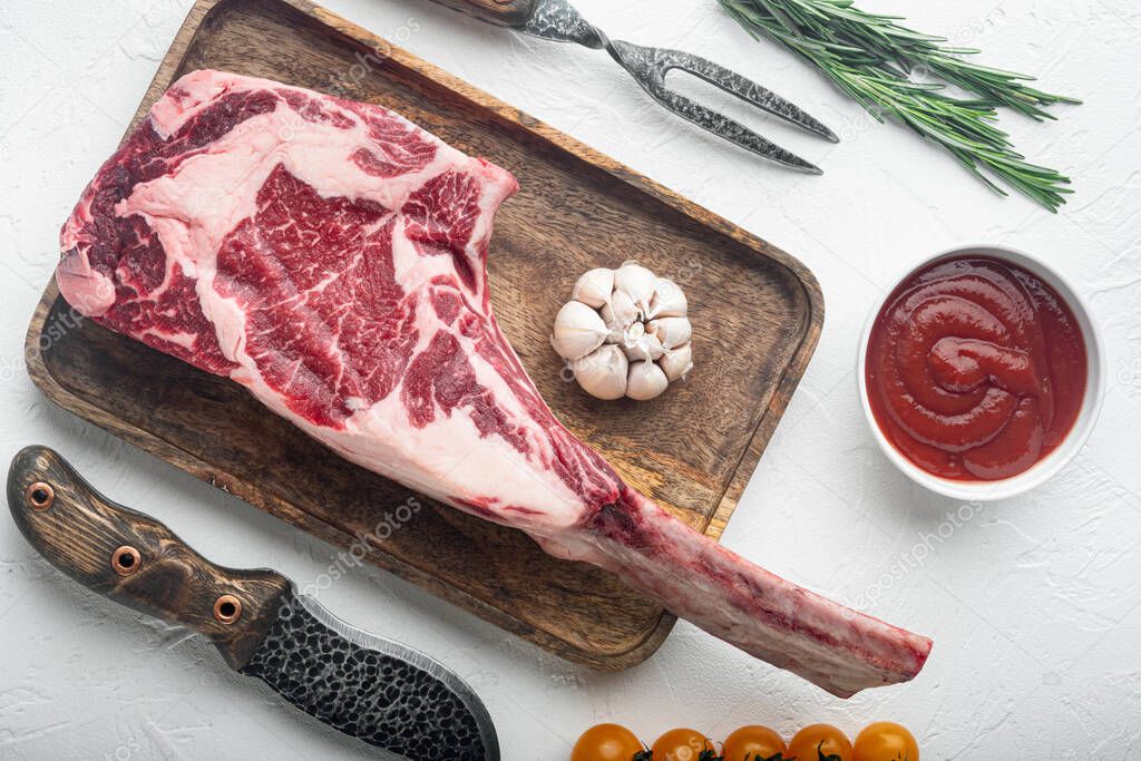 Raw fresh tomahawk dry aged marbled beef chop steak set, with seasoning and herbs, on white stone  background, top view flat lay