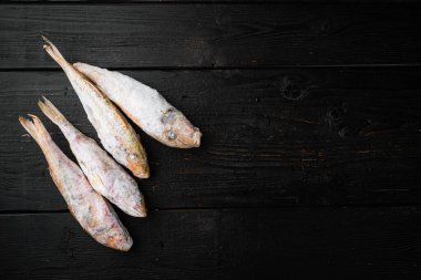 Donmuş keçi balığı çiğ balık seti, siyah ahşap masa arkaplanı, üst görünüm düz, metin için kopyalama alanı ile