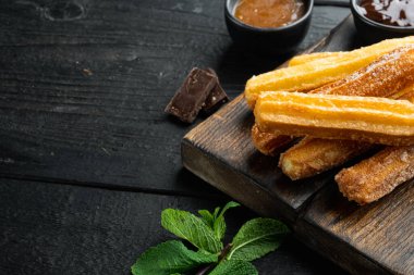 Tipik İspanyol çerez churros, kızarmış hamur pastası genellikle çikolatalı karamelli acı sos setiyle servis edilir, siyah ahşap masa üzerinde metin ve kopyalanacak yer vardır.