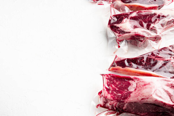 Plastic Market pack with fresh beef steak set, tomahawk, t bone, club steak, rib eye and tenderloin cuts, on white stone  background, with copy space for text