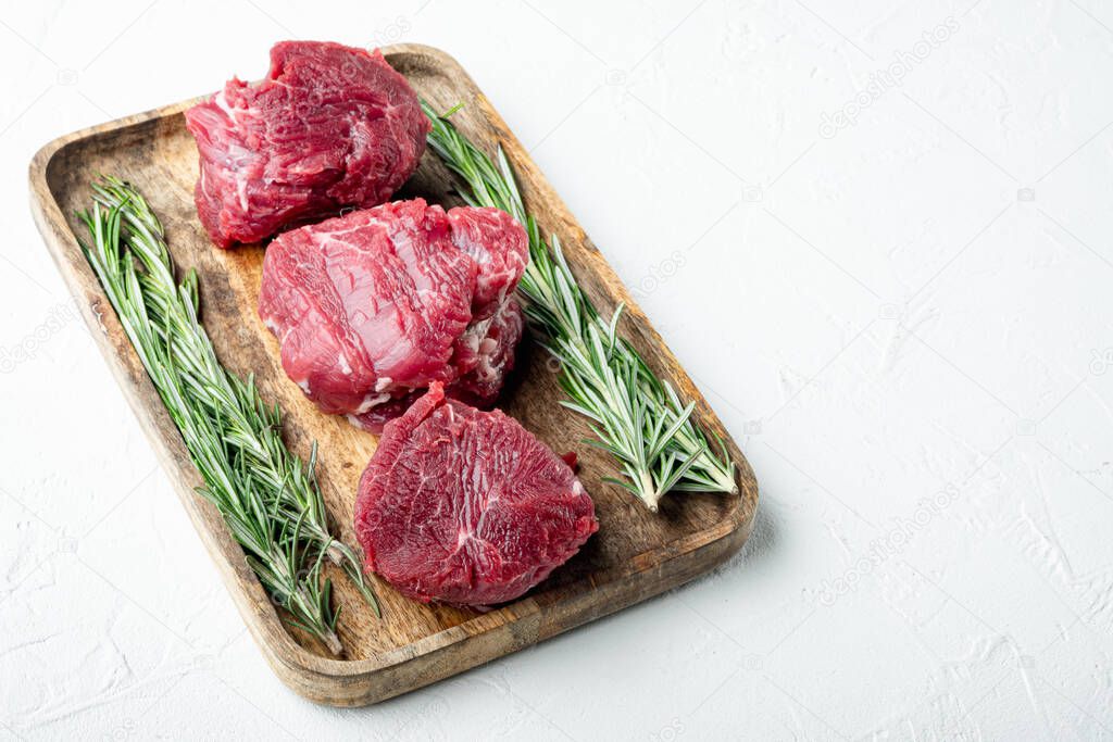 Raw filet mignon or eye steaks with herbs and spices set, on wooden cutting board, on white stone  surface, with copy space for text