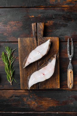 Çiğ halibut, tuzlu su balığı bifteği seti, malzemeler ve biberiye otları, eski siyah ahşap masa arka planı, üst düz yatıyordu
