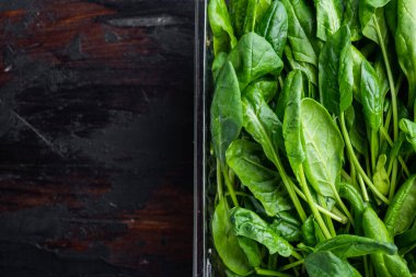 Taze ıspanak yaprakları seti, eski koyu ahşap masa zemininde, plastik pakette, üst görünüm düz yerde, metin kopyalama alanı için yer var