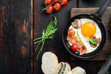Kızarmış yumurta ve kiraz domatesli ve kahvaltıda demir tavada ekmek, eski koyu ahşap masa zemininde, üst düz yerde, metin kopyalanacak yeri var.