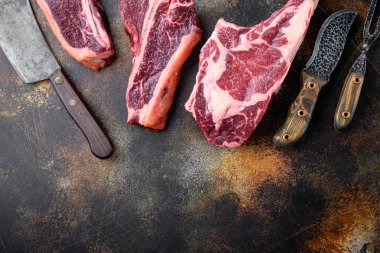 Kurumuş çiğ biftek biftek seti, tomahawk bifteği, biftek ya da biftek ve eski kasap satırı bıçağıyla eski kasap satırı bıçağı, eski siyah kırsal arka planda, üst manzara düz, metin için yer var.