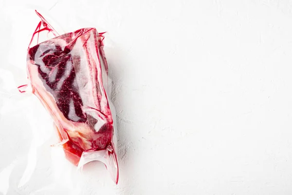 Fresh marbled meat black angus steak in vacuum plastic bag for sous vide set, on white stone  surface, with copy space for text