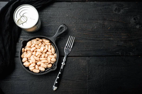 White canned kidney beans set, with metal can, in cast iron frying pan, on black wooden table background, top view flat lay, with copy space for text