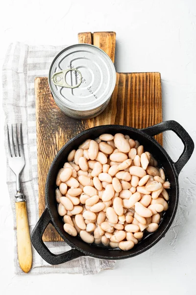 White canned kidney beans set, with metal can, in cast iron frying pan, on white stone  surface, top view flat lay