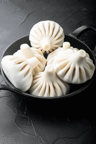 Delicious baozi, Chinese steamed meat bun set, in frying cast iron pan, on black stone background