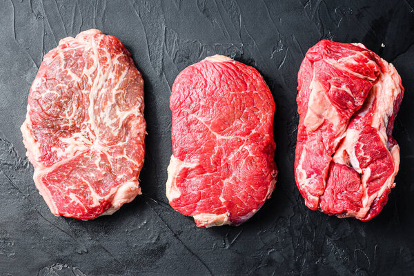 Set of alternative cuts beef steaks, top blade, rump and chuck roll, on black textured background, top view