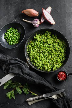 İngiliz lapa bezelyesi kızartma tavası ve bezelye kabında naneli arpacık soğanı biberi ve tuz ile siyah taş yüzeyinde organik keto yemeği çatal ve bıçakla üstten görünüşü..