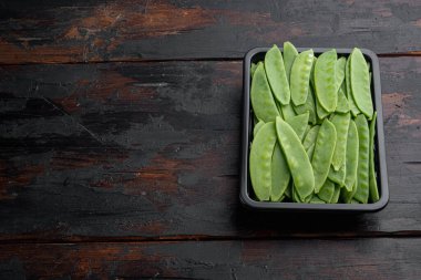 Şekerli bezelyeler, taze olgun bebek kabukları, plastik kabın içinde, eski koyu ahşap masa zemininde, kopyalanacak yeri ve metin için yeri olan.