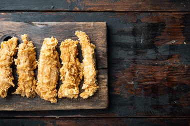 Koyu ahşap zemin üzerinde çıtır tavuk eti, düz uzanmış, metin için yeri var..