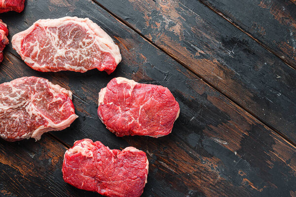 Set  of organic raw beef steakes rump, chuck roll and top blade  cut  on old rustic dark wooden background, top view with space for text