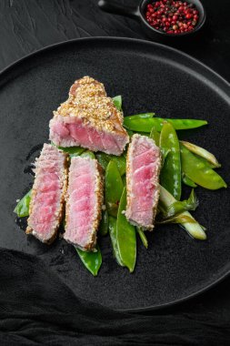 Izgara Ahi Ton Balığı Bifteği. Taze soğan ve bezelye, tabakta, siyah taş zemin üzerinde.