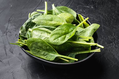 Taze yeşil bebek ıspanak yaprakları yığını, siyah taş arka planda, kasede.