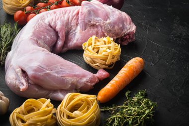 Çiğ tavşan eti ve pişirme malzemeleri güveç tagliatelle seti, siyah taş zemin üzerinde, metin için kopyalama alanı ile