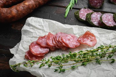 Koyu ahşap arka planda otlarla dilimlenmiş kurutulmuş sucuk, fuet ve diğer sosisler..