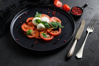 Kiraz domatesleri, mozzarella bufalo peyniri fesleğen, pesto sosu ve siyah tahtadaki baharatlar. İtalyan geleneksel Caprese salata malzemeleri. Akdeniz yemekleri.