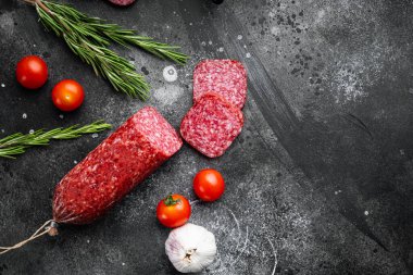 Geleneksel tütsülenmiş salam sosisi, baharatlar seti, siyah taş masa arkaplanı, üst görünüm düz, metin alanı için kopyalama alanı