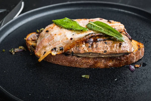 Ekmeğin üstünde domuz pastırması ve soğan. Siyah yüzeyde tabakta pişmiş yemek..